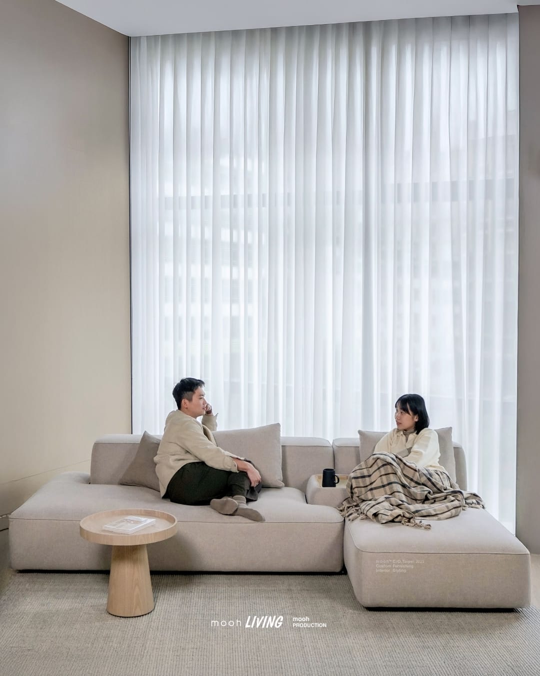 mooh Living 佛林斯｜三人沙發生活情境,一對男女輕鬆坐在沙發上對視交談,沙發中間放有木托盤與黑色馬克杯